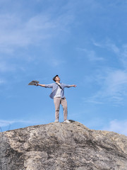 Asian tourist standing on the rock and raising hands with blue sky background,