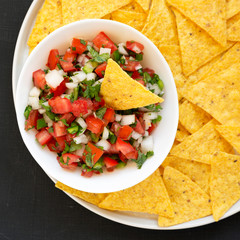 Pico de Gallo with gluten free tortilla chips on a black surface, top view. Flat lay, overhead, from above. Close-up.