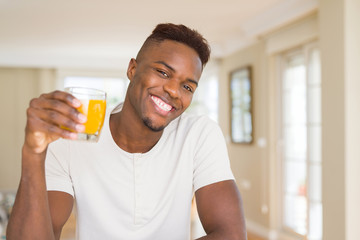Handsome young african man drinking a glass of fresh natural orange juice and smiling