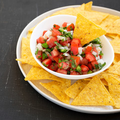 Pico de Gallo with gluten free tortilla chips on a black surface, side view. Close-up.