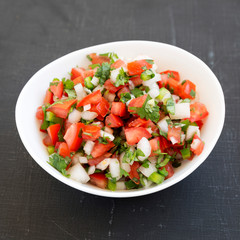 Pico de Gallo in a white bowl on a black surface, low angle view. Closeup.