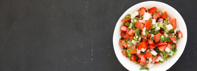 Pico de Gallo in a white bowl on a black background, top view. Overhead, from above, flat lay....