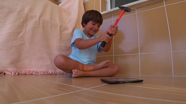 HD Smiling child crushes his tablet PC with a hammer, slow motion 