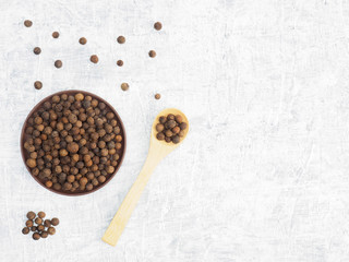 Spices and herbs help maintain good health and improve appetite, top view on white concrete background. Allspice in clay plate and in wooden spoon. Modern apothecary, naturopathy and ayurveda concept.