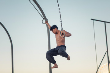 A young man athlete working out on traveling rings on muscle beach, Santa Monica, California