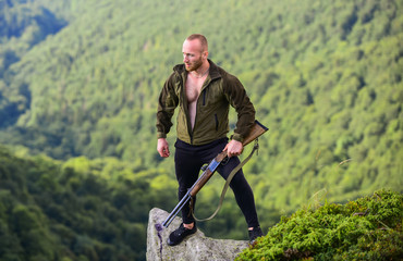Poacher stand on edge of cliff. Poaching concept. Man brutal poacher with weapon natural landscape...