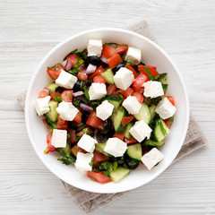Homemade Shepards salad with cucumbers, feta and parsley in a white bowl on a white wooden background, top view. From above, overhead, flat lay. Close-up.