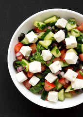Homemade Shepherd's salad with cucumbers, feta and parsley in a white bowl on a black surface, top view. From above, overhead, flat lay. Close-up.