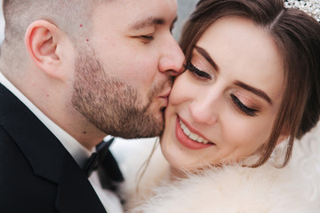 Wedding couple in winter time walking outside. Close up of handsome bearded groom kiss beautiful bride
