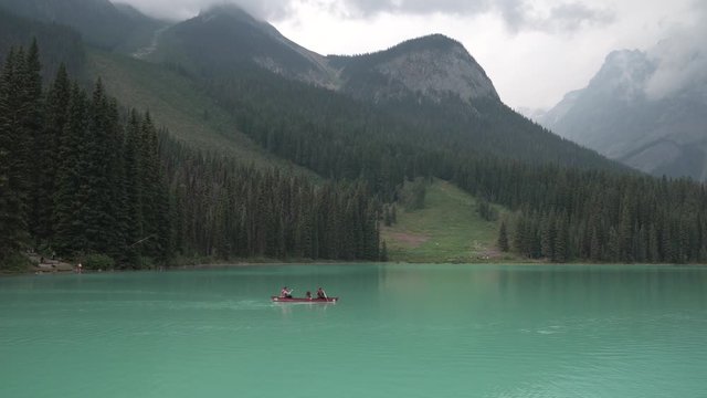 A wide angle shot of a family canoeing across an emerald lake in British Colombia