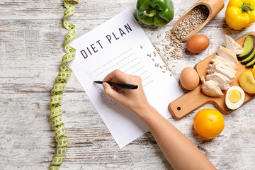 Woman writing something on sheet of paper with diet plan, top view - obrazy, fototapety, plakaty