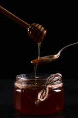 Liquid May honey flows down into spoons in a jar. Sweet cascade on a black background.