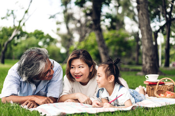 Portrait of happy grandfather with grandmother and little cute girl enjoy relax in summer park.Young girl with their laughing grandparents smiling together.Family and togetherness