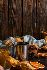 Iron mug with black coffee, spices, dry oranges, on a background of a scarf, dry leaves on a wooden table. Autumn mood, a warming drink. Copy space.