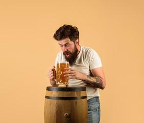 Craft beer at restaurant. Surprised man with wooden barrel of beer and mug of beer. Brewer. Oktoberfest. Holliday, drinks, alcohol, leisure concept. Bearded man hold glass and barrel with craft beer.