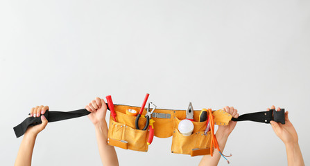 Female hands holding electrician's belt with tools on light background