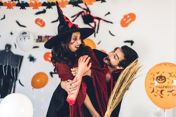 Couple having fun holding pumpkins and wearing dressed carnival halloween costumes and makeup posing with bats and balloons on background at the halloween party.Halloween holiday celebration concept