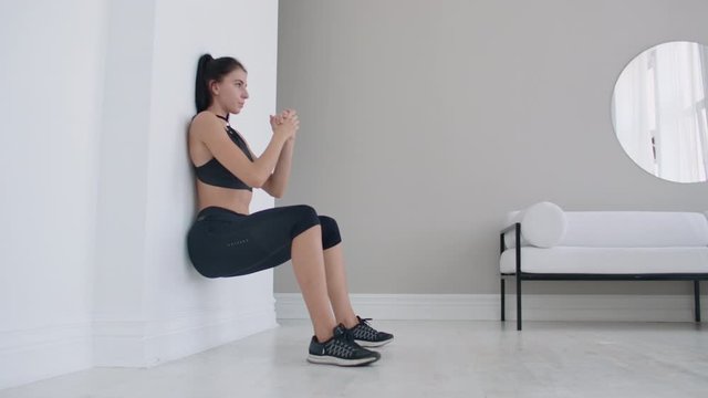 A woman in a static position carries out a grueling exercise leaning against a wall in a sitting position. Endurance training