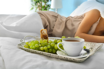 Tray with tasty breakfast on bed of young woman
