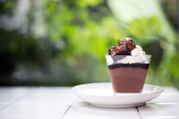 Closeup dark chocolate mousse in glass put on white desk with blur nature background. 