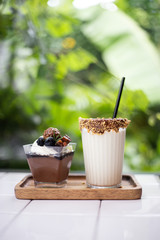 Closeup white chocolate milk with  chocolate mousse cake put on white desk with blur nature background. Snack and beverage in coffee cafe.