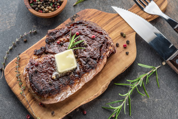 Medium rare Ribeye steak with herbs and a piece of butter on the wooden tray.