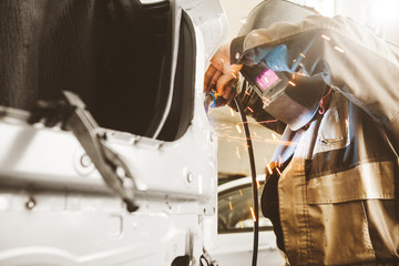 Professional car body repair, welding of auto body. Industrial worker welds metal elements of...