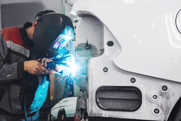 Man wearing protective mask while repairing rear car body with welding machine. Weld of vehicle.