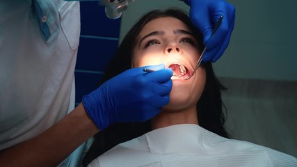 dentist in medical gloves and mask cures patient woman's teeth using dental mirror and dam during appointment in dental clinic - sealing