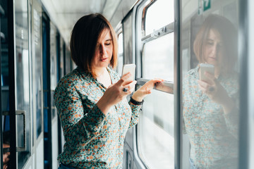 Attractive dark-haired woman in a shirt with a phone in her hand stands in the vestibule of a train...
