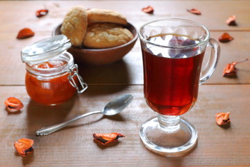 A glass mug of black tea with a glass bowl of homemade peach jam on a wooden table. 