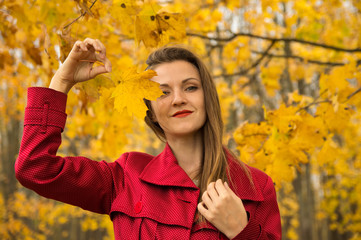 Warm autumn. Beautiful girl in a red coat holds yellow leaves in the autumn park.