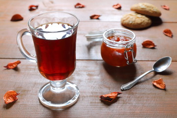 A glass mug of black tea with a glass bowl of homemade peach jam on a wooden table. 