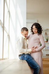 Pregnant woman with husband stands near window.