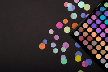 Above view of eyeshadow palette on a black background with scattered confetti