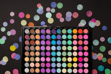 Eyeshadow palette on a black background with scattered confetti. Top view. Flat lay