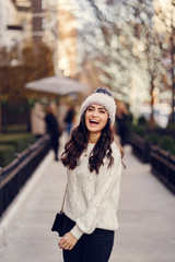 Elegant girl walk in a winter city. Woman in a white knited sweater. Beautiful lady with dark hair.