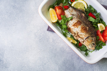 Baked carp fish with vegetables and spices in a baking tray with copy space.