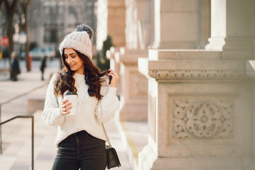 Elegant girl standing in a winter city. Woman in a white knited sweater. Beautiful lady with dark hair.