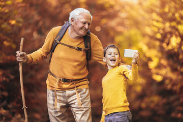 Grandfather and grandson hiking together in autumn park, make selfie photo.