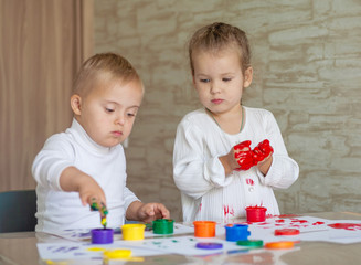 Little children paint with paints. The kids got their hands dirty in gouache. A cute girl and a boy with Down Syndrome are creative.