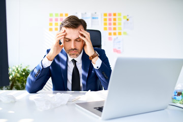 Businessman sitting in office suffering from headache holding head in pain