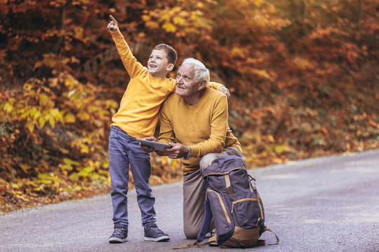 Senior man reading map on digital tablet with grandson in forest walk.