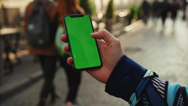 Close up man hand using phone with vertical green screen background sunlight road car city blurred internet chrome outdoor cellular smartphone scrolling tapping communication slow motion