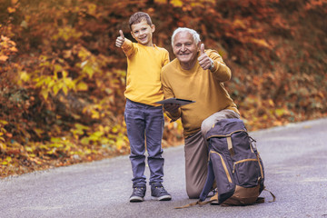 Senior man with grandson in forest walk, showing thumbs up.