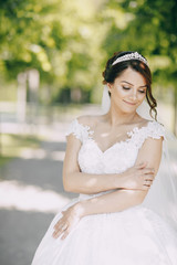 Fototapeta na wymiar beautiful bride in a magnificent white dress and a crown on his head standing in a park and holding a bouquet of flowers in hand