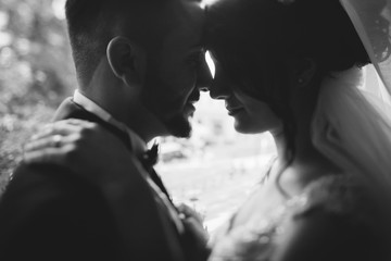 A beautiful young Turkish man wearing a black suit and a beard standing near windows along with his beautiful bride in a white dress