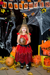 A child, a little girl in the shape of a witch on a broomstick, poses against the backdrop of scenery of cobwebs, pumpkins and autumn leaves on a Halloween holiday.