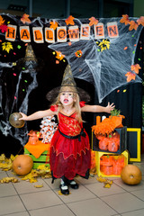 A child, a little girl in the shape of a witch on a broomstick, poses against the backdrop of scenery of cobwebs, pumpkins and autumn leaves on a Halloween holiday.