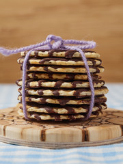 Chocolate cookies on wooden plate on table covered by blue tablecloth. Vertical close up view.